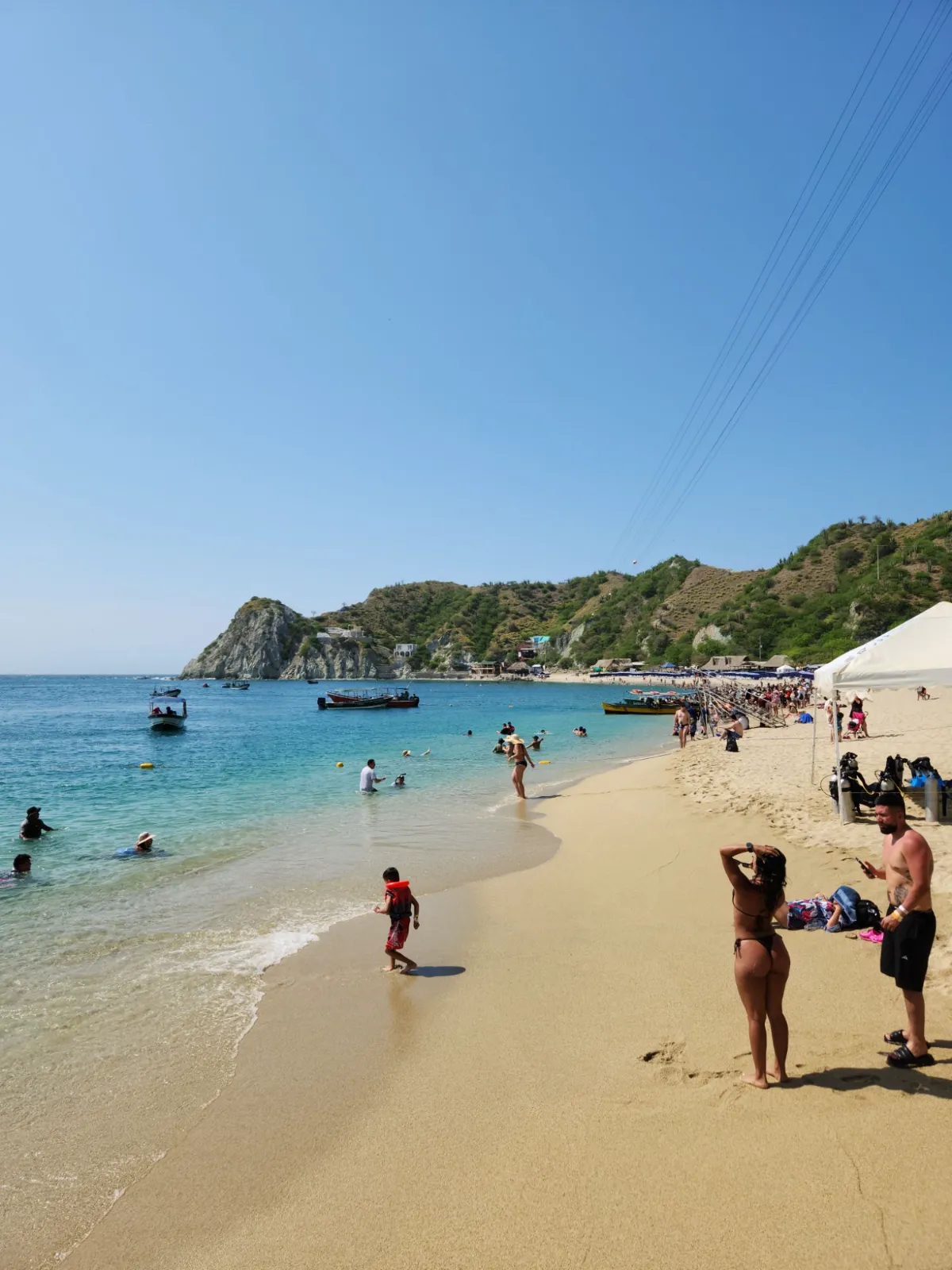 Orilla de arena dorada de Playa Blanca con agua turquesa, lanchas y un cerro rocoso al fondo.