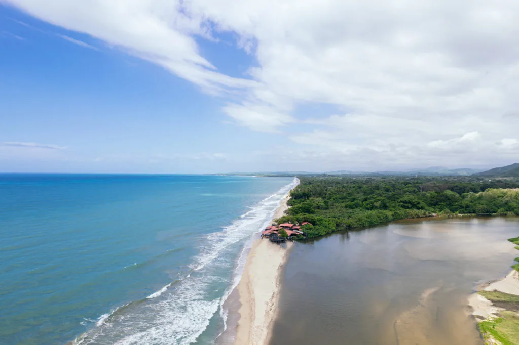 Vista aérea de Buritaca: playa larga, el mar turquesa y el río llegando al mar entre la vegetación.