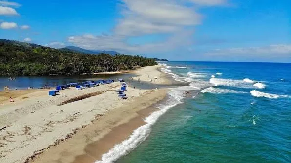 Playa de Palomino con carpas azules, el río a un lado y las olas del mar Caribe al otro.